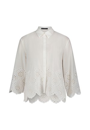 Blouse blanche avec col, manches longues et ourlet festonné complexe présentant des motifs floraux découpés. Fabriquée en tissu léger.