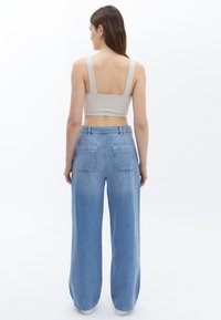 Ljusgrå, ribbad kort topp med breda axelband, parat med högmidjade ljusblå vida jeans som har två bakfickor.