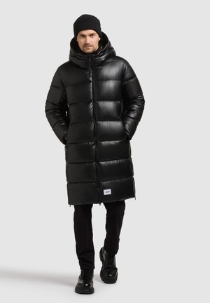 Svart puffjacka med blanka yta, huva och framtida dragkedja. Har vertikalt quiltade sektioner och en logotyp patch i fållen.