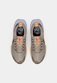 Beige sportssko med grå detaljer, som har overdel av mesh, teksturert såle og oransje høydepunkter på snøringen og hæltappen.