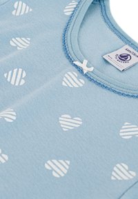 Βαμβακερό φορμάκι ανοιχτό μπλε με μοτίβα καρδιάς σε λευκές ρίγες, με στρογγυλή λαιμόκοψη και κυματιστά τελειώματα, διακοσμημένο με ένα μικρό φιόγκο.