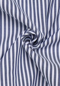 Tessuto di twill di cotone con strisce diagonali blu navy e bianche, caratterizzato da una texture liscia e una leggera lucentezza, disposto in un motivo piegato.