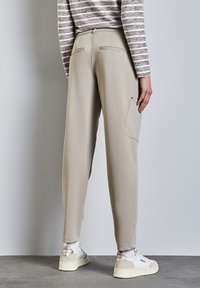 Ljust beige tapered byxor med elastiskt midjeband, två bakfickor och en sidficka. Slät tyg och avslappnad design.