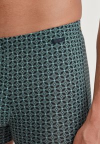 Heren boxershorts in donkergroen met een geometrisch patroon in lichtblauw en zwart. Zachte stof met een CALIDA-logo label op de tailleband.