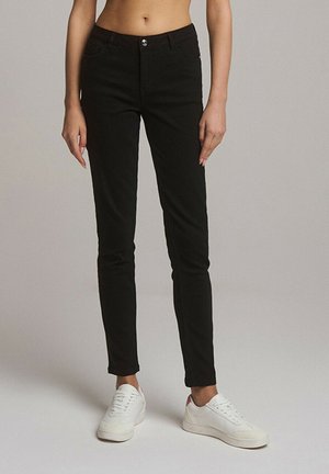 Czarne jeansy slim fit z wysokim stanem, z przodu z zapięciem na guzik i zamek błyskawiczny, o minimalistycznym designie; zestawione z białymi sneakersami.