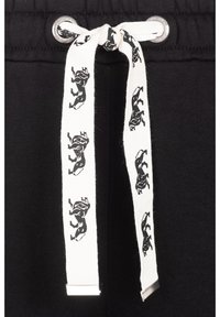 Black sweatpants feature a white drawstring with black animal print and metal tips, emphasizing a contrasting design and detailed texture.