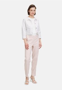 Weiße, verkürzte Jeansjacke über einem weißen T-Shirt, kombiniert mit hellrosa, maßgeschneiderten Hosen und weißen, sandalenartigen High Heels.