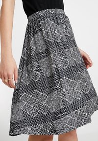 Svartvit mönstrad kjol med geometriska former, samlad elastisk midja och en flödande A-linjeform. Slät tygtextur.