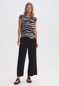 Top a maniche corte a righe bianche e nere con una vestibilità comoda, abbinato a pantaloni neri a gamba larga e sandali piatti neri. Tessuto morbido.