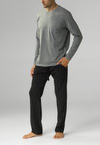 Szara koszulka z długim rękawem z kieszonką na piersi, zestawiona z czarnymi spodniami z białym okrągłym wzorem i elastycznym pasem z troczkami.