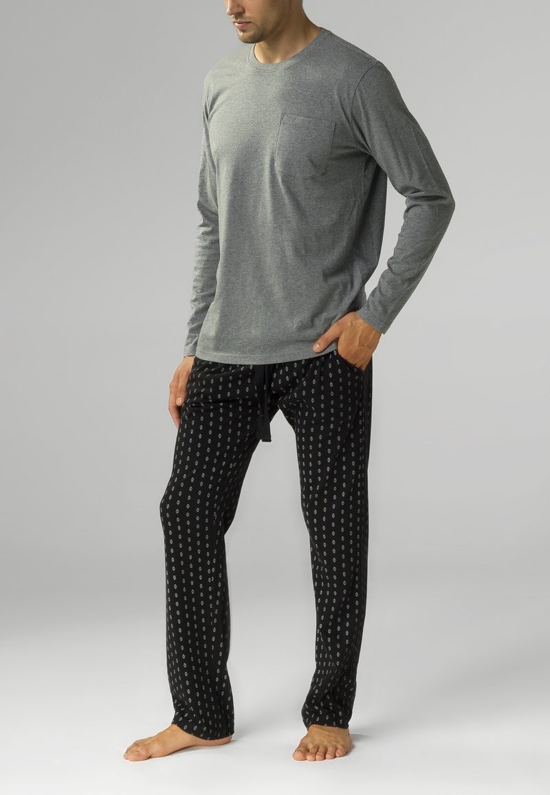Szara koszulka z długim rękawem z kieszonką na piersi, zestawiona z czarnymi spodniami z białym okrągłym wzorem i elastycznym pasem z troczkami.