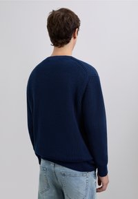 Granatowy sweter z dzianiny o fakturowanym wzorze, z prążkowanymi mankietami i obrębem. Luźny krój, przedstawiony od tyłu na jednolitym tle.