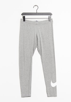 Jasnoszare legginsy sięgające do kostek z białym logo Nike na dolnej lewej części nogi, zawieszone na czarnym wieszaku na białym tle.