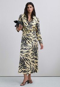 Vestido de manga larga con un estampado de rayas de tigre en amarillo y negro, con un cuello tipo solapa y una cintura ceñida. Combinado con un bolso de mano negro.