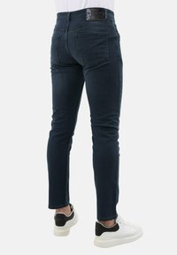 Donkerblauwe denim jeans met een slim fit, met een soepele textuur, achterzakken en een leren logo patch op de tailleband. Witte sneakers.