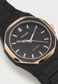 Montre en polycarbonate noire avec un boîtier octogonal en or rose, un cadran noir, des index horaires roses et un bracelet en silicone. Présente un design minimaliste.