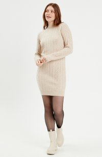 Robe pull en beige clair avec un motif texturé, des manches longues et un ourlet côtelé, associée à des bottines aux chevilles de couleur crème.
