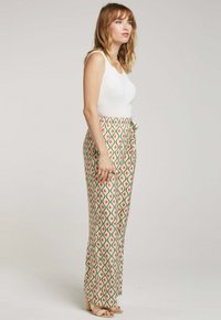 Pantalons fluides à motifs avec un design vert, rouge et blanc ; dotés d'une taille à cordon de serrage et de jambes larges ; associés à un débardeur blanc ajusté.