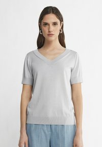 Hellgrauer, kurzärmeliger V-Ausschnitt-Pullover mit glatter Textur und geripptem Saum. Verfügt über eine lockere Passform und minimale Nahtdetails.