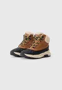 Bruine en zwarte winterboots met beige schapenvacht lining, dikke beige zolen en zwart-geel gestreepte veters op een witte achtergrond.