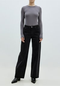 Maglietta grigia a maniche lunghe a coste abbinata a jeans neri a gamba larga e tacchi neri a punta. L'outfit presenta linee pulite e dettagli minimi.