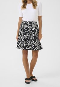 Jupe A-line noir et blanc avec un motif de feuilles, fabriquée en tissu léger. Associée à un haut blanc ajusté et des sandales noires.