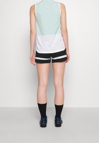 Top sin mangas verde menta y blanco combinado con pantalones cortos a rayas negras, complementado con calcetines negros y zapatos con detalles azules.