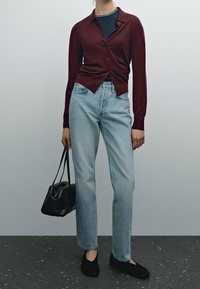 Bordeaux cardigan over een zwarte top, lichtblauwe recht gesneden jeans, zwarte tas en zwarte schoenen. Gladde materialen, getailleerd ontwerp en casual stijl.
