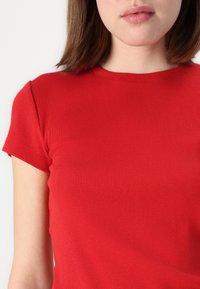 Rød ribbet kortærmet top med rund halsudskæring og tætsiddende design, der fremhæver en glat tekstur og blødt stof.