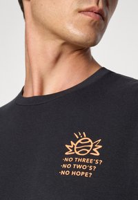 Sort bomuld t-shirt med et grafisk design, der viser en orange tennisbold og tekst på brystet. Rund halsudskæring og korte ærmer.