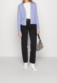 Cardigan lila claro, camisa blanca, jeans negros de cintura alta, botines blancos y un bolso a rayas blanco y negro.