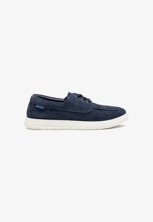 Scarpa casual stringata in camoscio blu navy con suola in gomma bianca, tallone basso ed etichetta del marchio Docksteps sul lato.