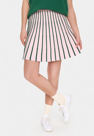 Jupe plissée avec des rayures verticales roses et vertes, réalisée en tissu léger. Associée à des baskets blanches et des chaussettes beige clair.