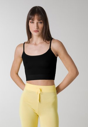 Sort cropped tank top med tynde stropper, ribbet kant, parret med gule joggers med snøre i blødt stof. Simpelt design, ingen mønstre.