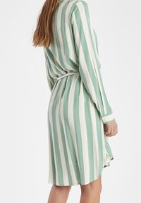 Abito a righe con strisce verticali verdi e bianche, maniche lunghe, colletto e dettaglio in vita legato. Realizzato in tessuto leggero.