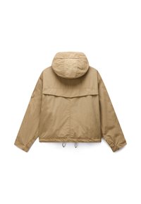 Beżowa lekka kurtka z kapturem, długimi rękawami, tylną klapą wentylacyjną, sznurkiem u dołu oraz okrągłą naszywką na lewym rękawie.