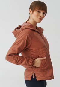 Veste légère matelassée couleur rouille avec capuche, poches latérales et poignets élastiques. Comprend un ourlet zippé pour un ajustement réglable.