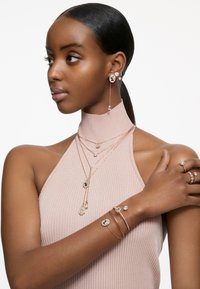 Neposlední vrstvené náhrdelníky, náušnice, prsteny a náramky z růžového zlata mají kulaté detaily s krystaly. Horní část má žebrovaný design s halter krkem.