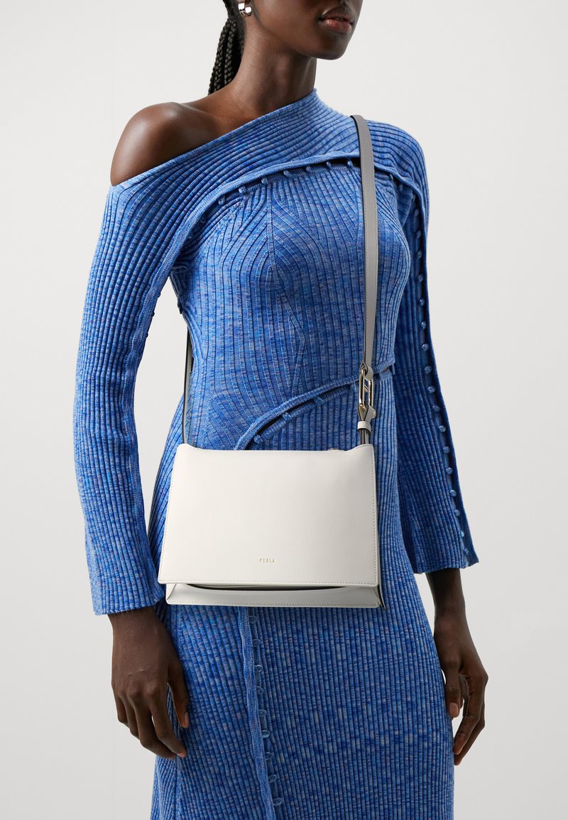 Borsa a tracolla bianca in pelle con superficie liscia, design minimalista e dettagli in metallo argentato. Indossata con un vestito blu a coste.