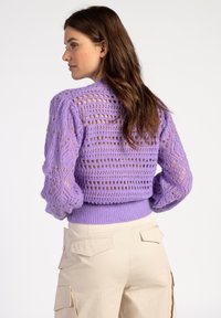 Paarse gebreide trui met een textuur, opengewerkte ontwerp, ballonmouwen en een geribde tailleband, gecombineerd met beige cargobroek.