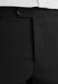 Pantalones negros de corte ajustado fabricados en un tejido texturizado, con cierre de un solo botón y diseño de frente plano.