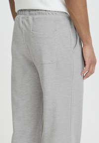 Un pantalon de survêtement gris en tissu doux présente une taille élastique, des poches latérales et une poche arrière près de la hanche droite.