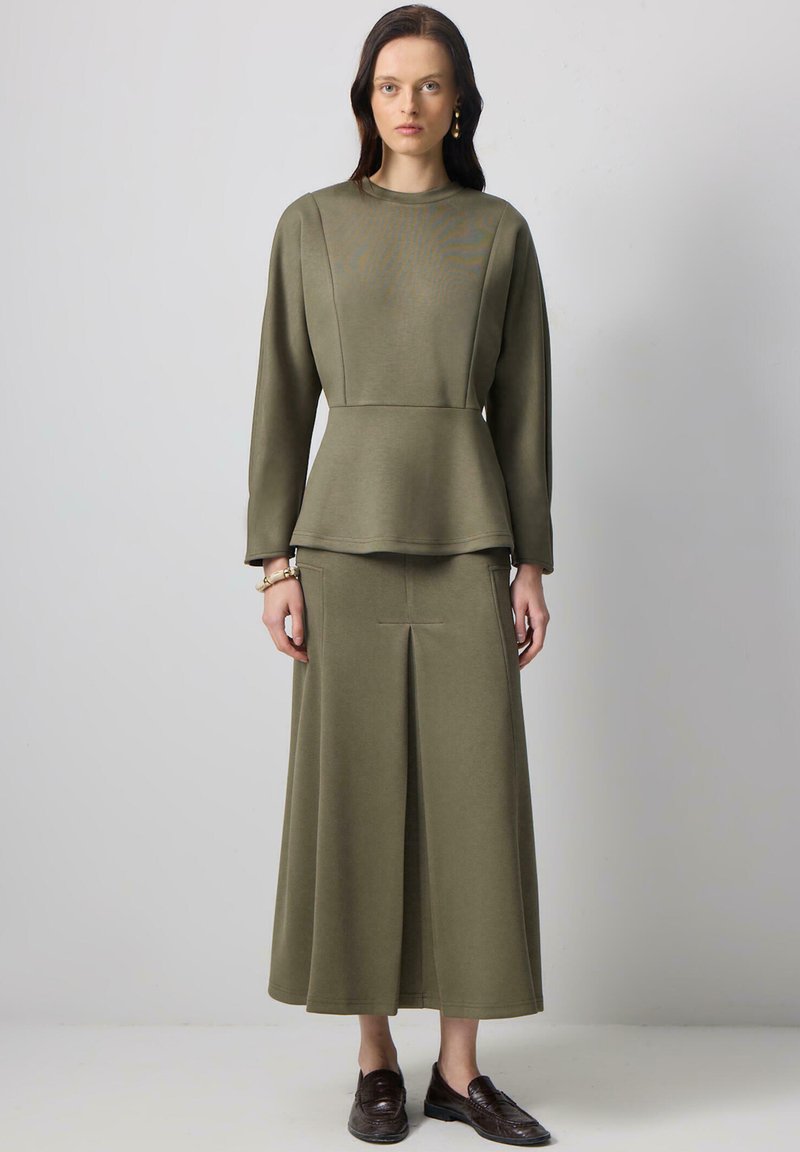 Olivově zelený, dlouhý rukáv, peplum top s odpovídajícími sukněmi, s hladkou texturou a jemnými sklady, v kombinaci s tmavými mokasíny.