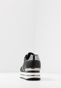 Czarny trampki o eleganckim designie, z błyszczącym, metalicznym obcasem i białymi akcentami na podeszwie. Obecny teksturowany materiał oraz detal z logo.