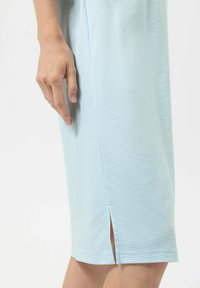 Niebieska sukienka w paski do kolan z bocznym rozcięciem, o gładkiej fakturze i dopasowanym kroju, pokazana z ręką przy tkaninie.