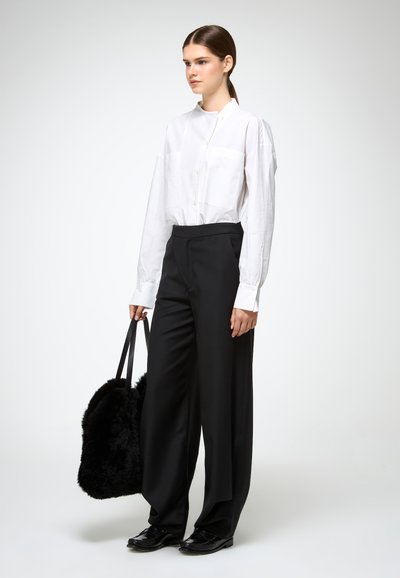 Ilgas baltas marškinėlių su sagomis priekyje ir kišene, derinamas su juodomis plačiomis kelnėmis su aukštu liemeniu ir juoda pūsta rankine.