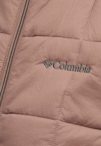 Κοντινό πλάνο ροζ μπουφάν με καπιτονέ σχέδιο, φερμουάρ και γκρι κεντημένο λογότυπο Columbia στο εμπρός μέρος.