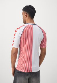 White sports jersey featuring red vertical stripes, red chevron accents on sleeves, and a round neckline for a contrast design.