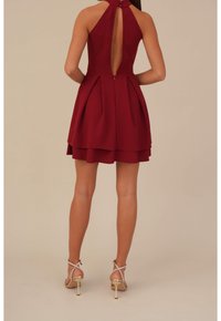 Burgundin lyhyt mekko, jossa on kaula-aukko, avoin selkä, pleated-hame ja piilotettu vetoketju. Sisältää hopeisia yksityiskohtia neliön muotoisissa korkokenkissä.