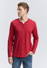Rød langærmet Henley-skjorte med struktureret mønster, tre-knaps stolpe, rund halsudskæring, parret med blå jeans.